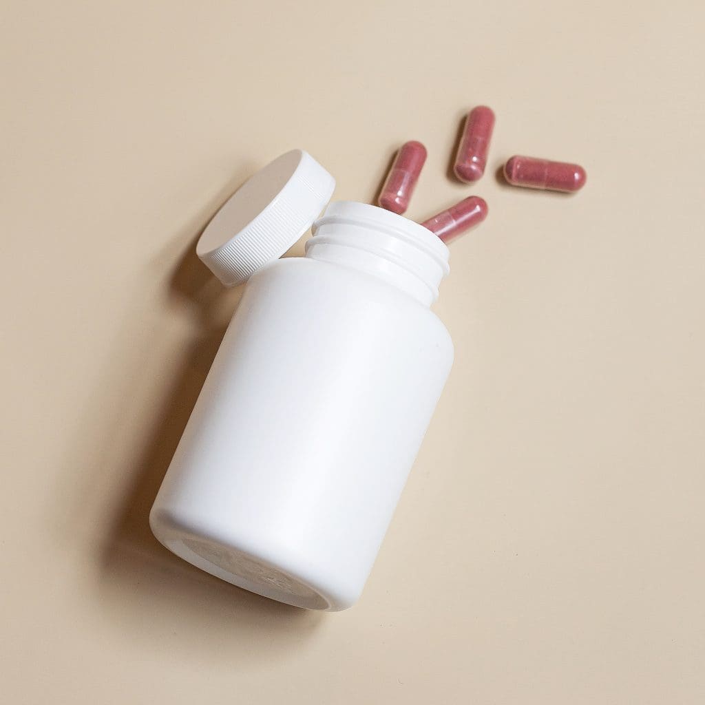 white bottle of vitamins on its side with no label tan capsules spilling out