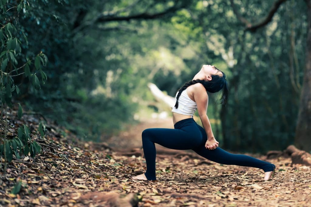 person stretching on a trail covered in fall leaves